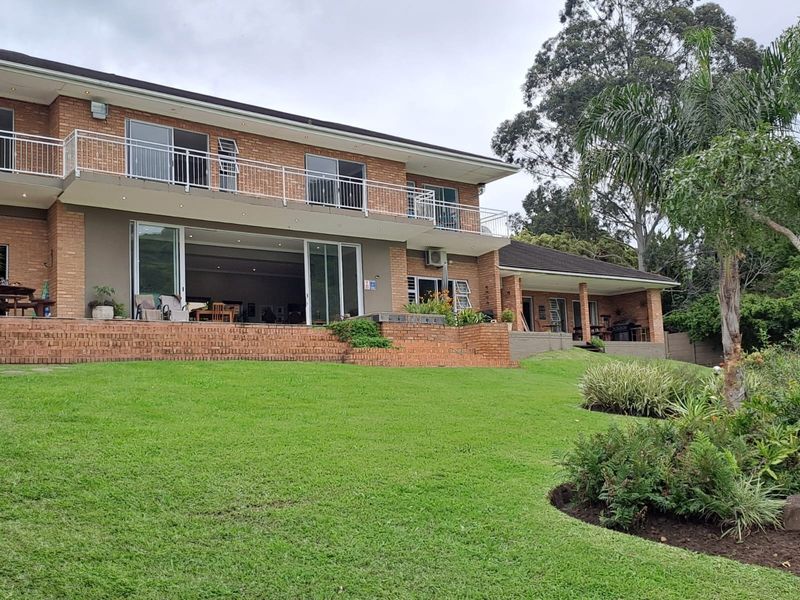 Rear view of a two-story brick guest house featuring a spacious lawn, a raised brick patio, and an upper-level balcony with sliding door access.