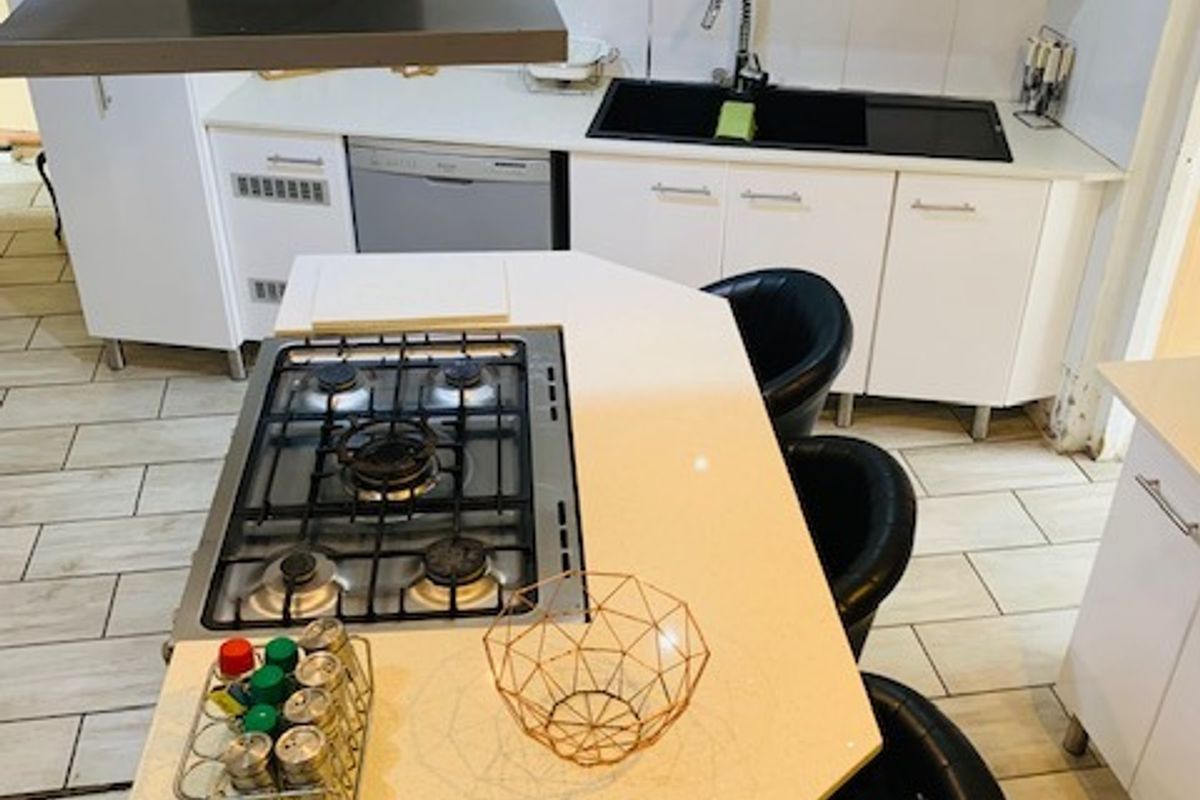 Modern kitchen featuring a central island with a built-in gas hob, white cabinetry, stone countertops, and a stainless steel extractor fan.