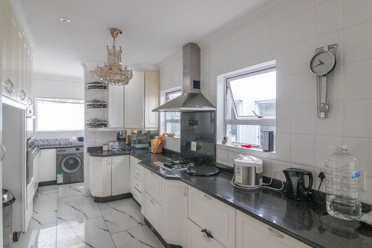 A functional kitchen featuring white cabinetry, dark granite countertops, a gas hob with extractor fan, and tiled flooring with integrated laundry space.