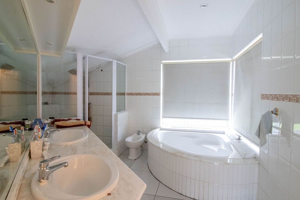 Spacious bathroom featuring a double vanity, corner bathtub, bidet, and separate shower enclosure with neutral tiled finishes.