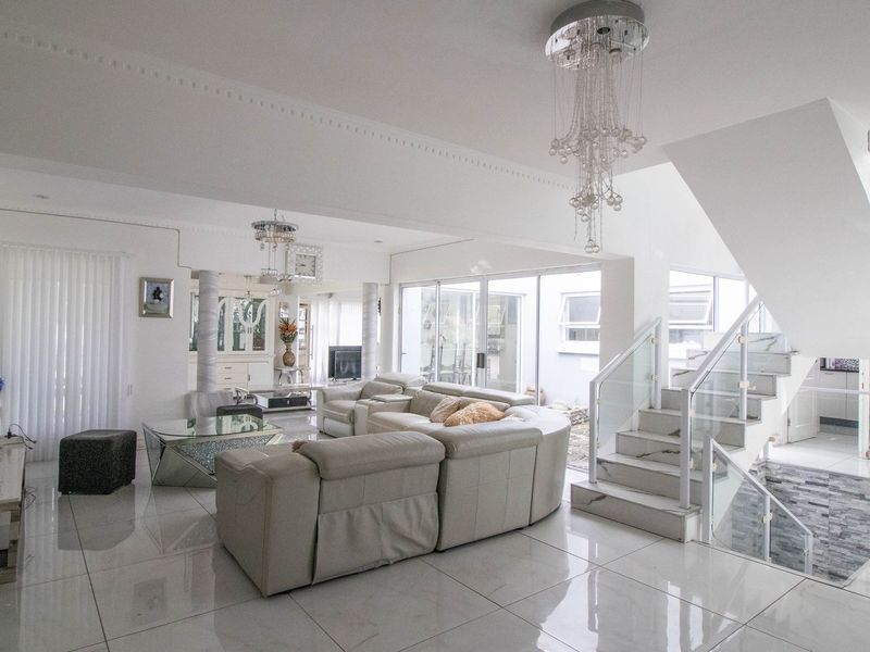 Spacious open-plan living area featuring polished porcelain flooring, a modern marble staircase with glass balustrades, and elegant crystal lighting fixtures.