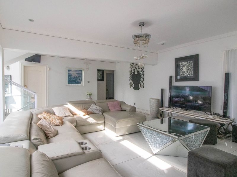 A bright and spacious living room featuring large sliding glass doors, polished tiled flooring, and elegant crown molding, creating a comfortable and inviting atmosphere.
