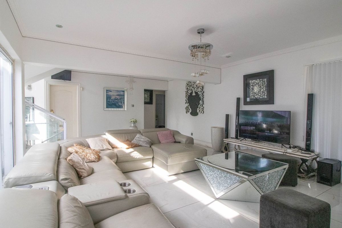 A bright and spacious living room featuring large sliding glass doors, polished tiled flooring, and elegant crown molding, creating a comfortable and inviting atmosphere.