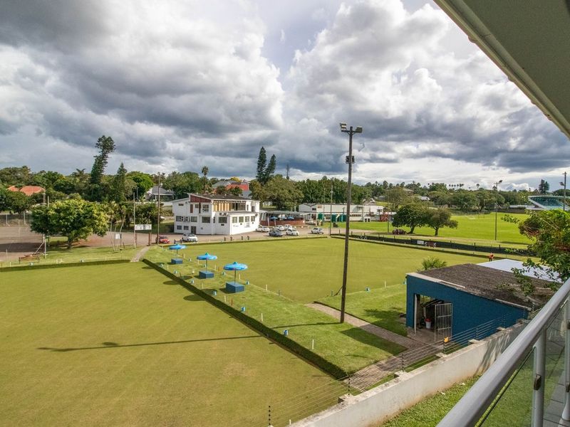 Elevated view from a balcony overlooking a local sports facility and bowling greens with surrounding neighborhood landscape.
