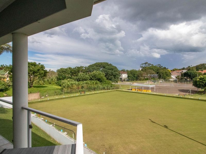 Elevated view from a balcony overlooking a well-maintained lawn and recreational area with surrounding greenery.