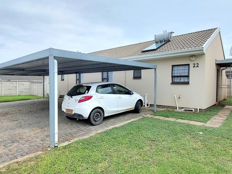 Front exterior view of the townhouse featuring a paved driveway, a metal carport, and a solar water heating system installed on the tiled roof.