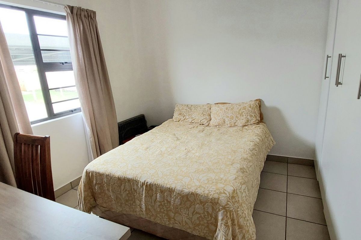 A functional bedroom featuring tiled flooring, built-in cupboards, and a window providing natural light.