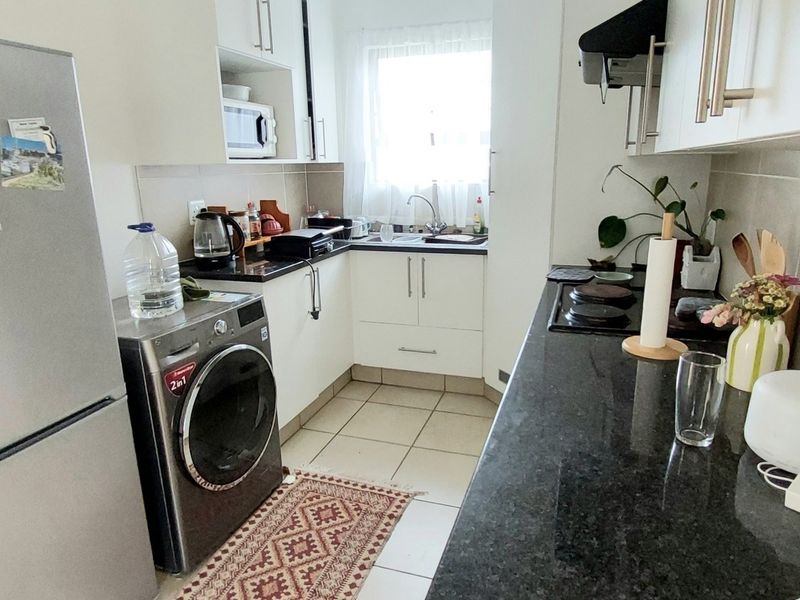 Compact kitchen featuring granite countertops, white cabinetry, tiled backsplash, and integrated cooking appliances in a functional galley layout.