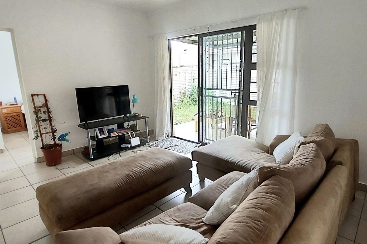 A living room featuring tiled flooring and a sliding glass door with a security gate, providing direct access to the outdoor patio area.