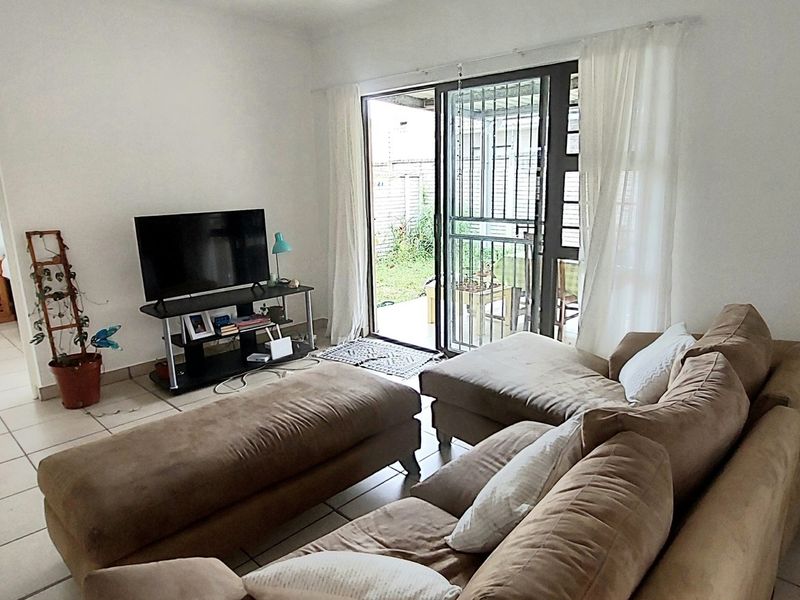 A living room featuring tiled flooring and a sliding glass door with a security gate, providing direct access to the outdoor patio area.