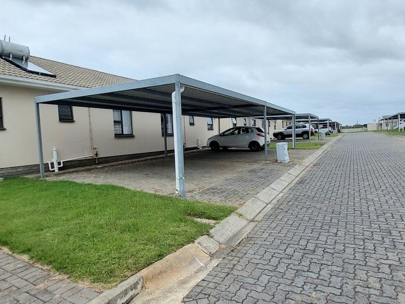 Front exterior view of a townhouse featuring a paved driveway, covered carport, and solar water heating system.