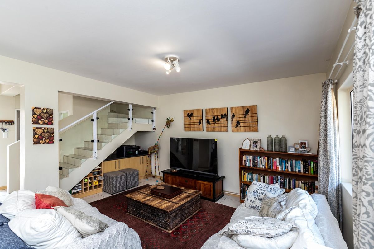 A comfortable living room featuring a modern staircase with glass balustrades and convenient built-in under-stair storage cabinetry.