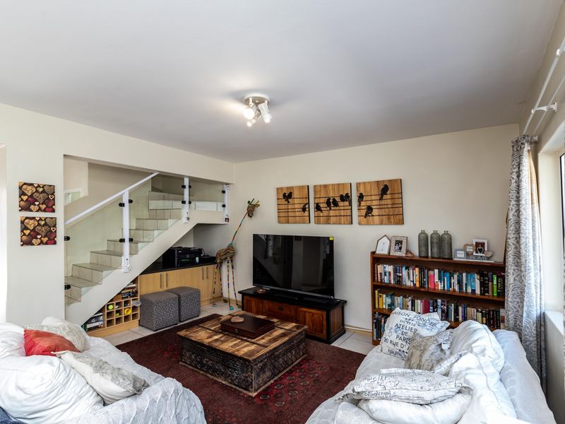 A comfortable living room featuring a modern staircase with glass balustrades and convenient built-in under-stair storage cabinetry.