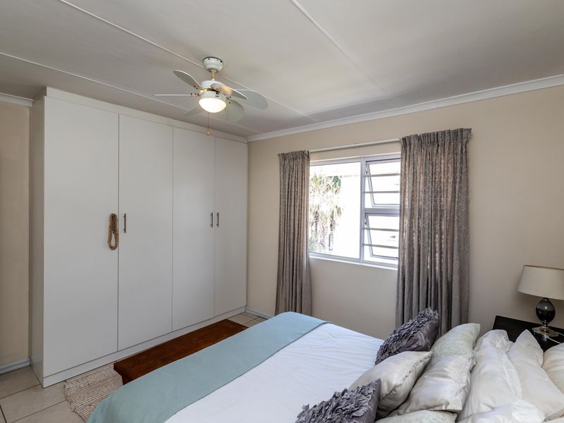 A well-lit bedroom featuring built-in cupboards, a ceiling fan, and tiled flooring, offering a functional and comfortable living space.