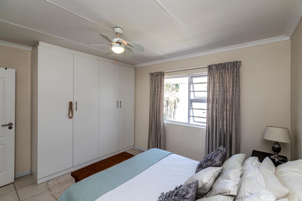 A well-lit bedroom featuring built-in cupboards, a ceiling fan, and tiled flooring, offering a functional and comfortable living space.