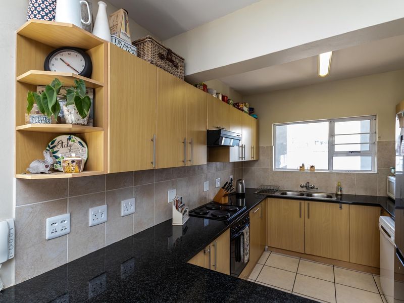 A functional kitchen featuring light wood-finish cabinetry, dark granite countertops, a double stainless steel sink, and tiled flooring with a neutral backsplash.