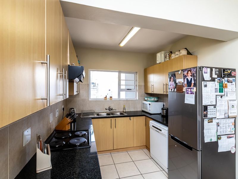 Functional kitchen featuring light wood cabinetry, dark countertops, tiled backsplash, and integrated electric hob with extractor fan.