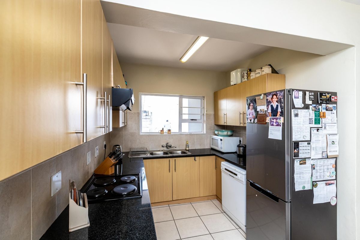 Functional kitchen featuring light wood cabinetry, dark countertops, tiled backsplash, and integrated electric hob with extractor fan.