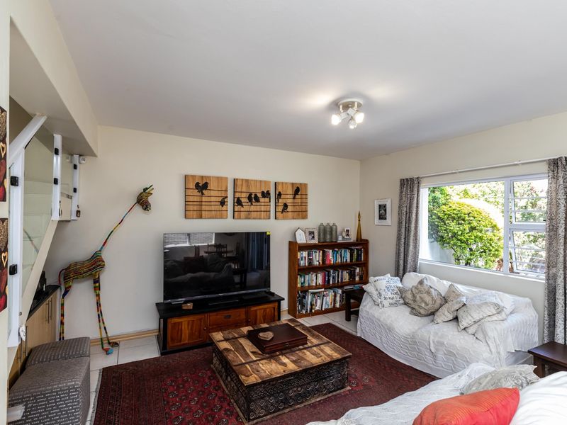A comfortable living room featuring a staircase, large window with natural light, and neutral wall finishes.
