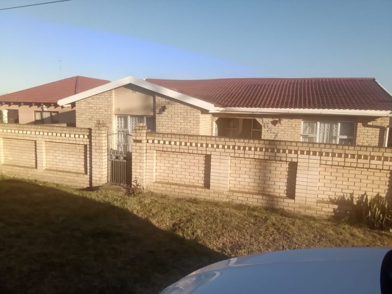 Front view of a single-story face brick house featuring a tiled roof and a secure perimeter wall with a gated entrance.