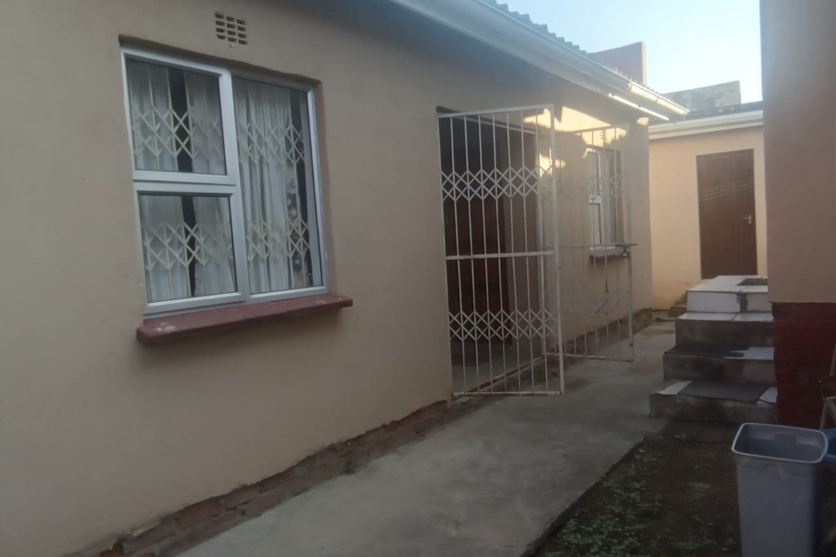Rear exterior view of the property featuring plastered walls, security gates, aluminium window frames, and a concrete pathway leading to tiled steps.