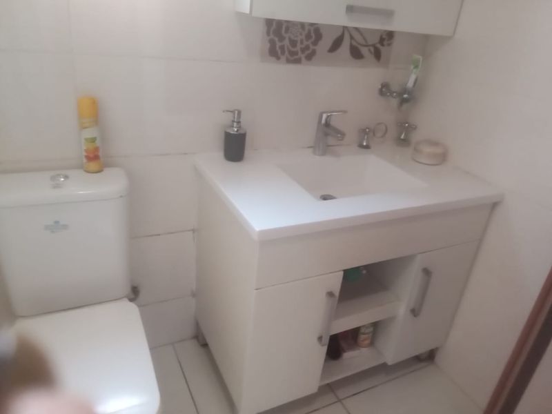 A compact bathroom featuring a white vanity cabinet with a basin, mixer tap, and a standard toilet with tiled walls and flooring.