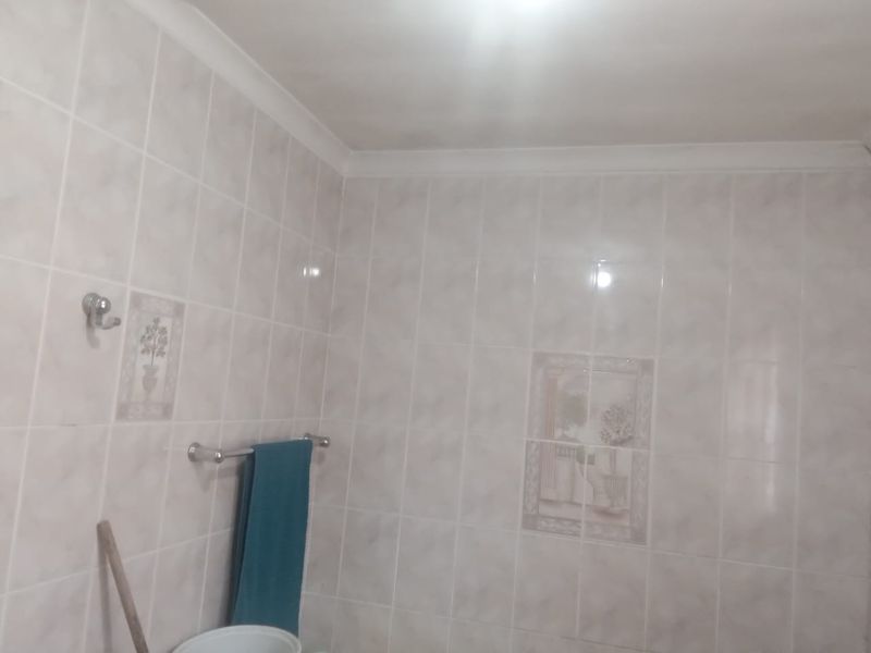 A functional bathroom space featuring neutral ceramic wall tiles with decorative accent tiles, a towel rail, and a robe hook.