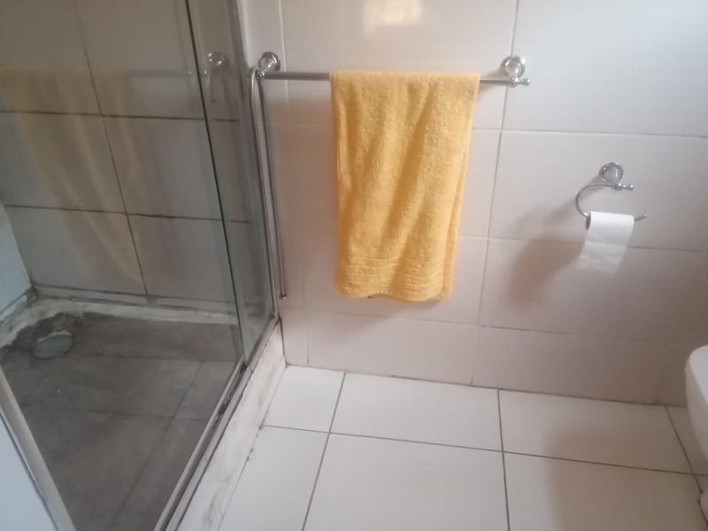 A functional bathroom featuring a glass-enclosed shower, tiled flooring, and wall tiling, requiring some maintenance to address grout and surface wear.