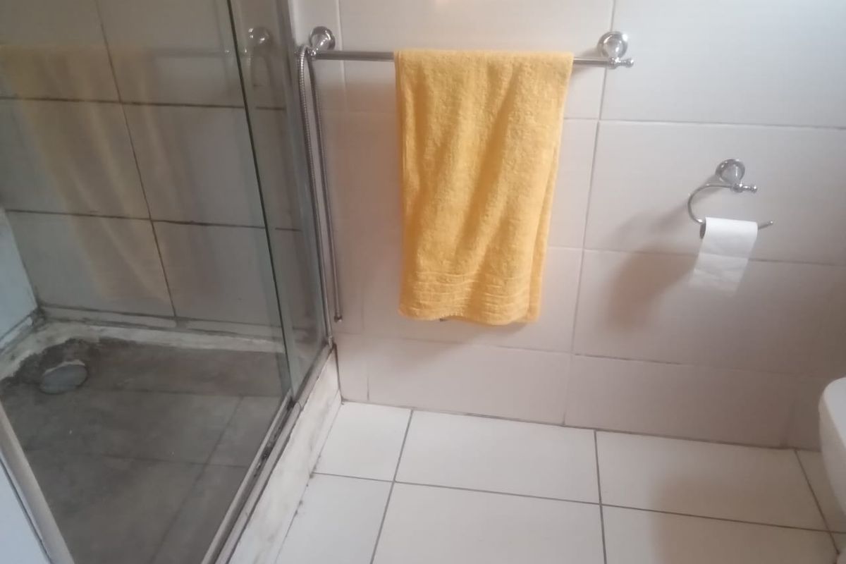 A functional bathroom featuring a glass-enclosed shower, tiled flooring, and wall tiling, requiring some maintenance to address grout and surface wear.