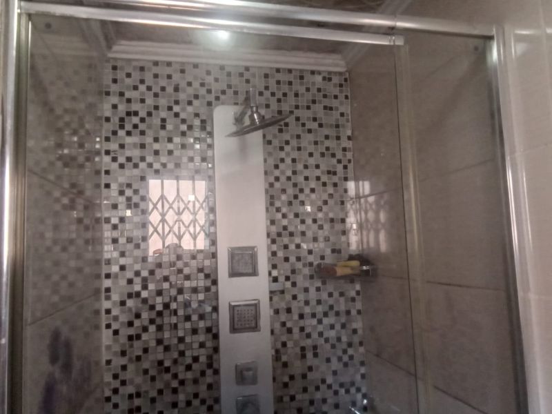 A bathroom shower stall featuring a modern shower panel with rainfall head, body jets, and decorative mosaic wall tiling.