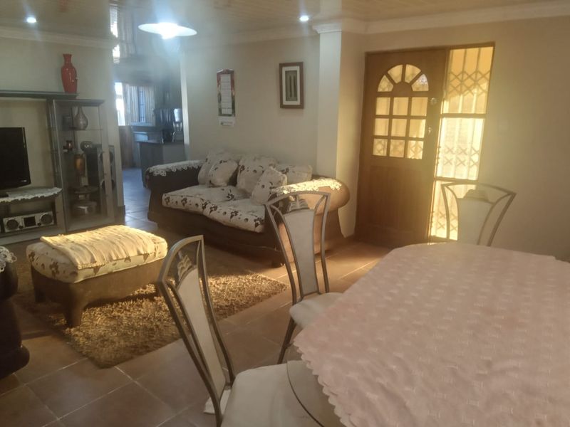 Open plan living and dining area featuring tiled flooring, timber panelled ceilings, and a classic timber entrance door with integrated security gate.