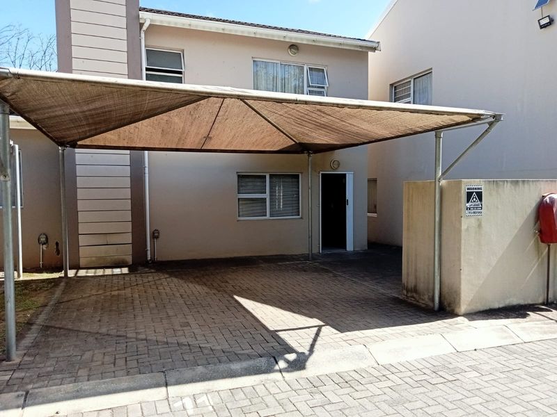 Front exterior view of the apartment featuring a paved driveway, a shade cloth carport, and a secure boundary wall.