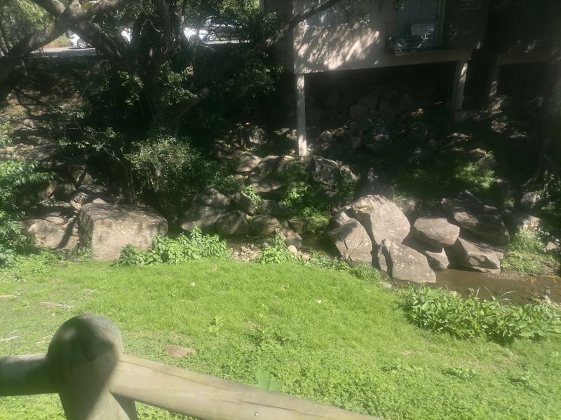 A view of the rear garden area featuring natural rock landscaping, a grassy slope, and a timber safety railing.