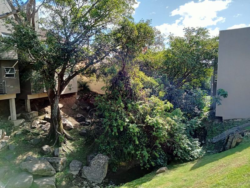 Rear exterior view of the apartment complex showing a sloped garden area with mature trees and visible soil erosion near the building foundation.