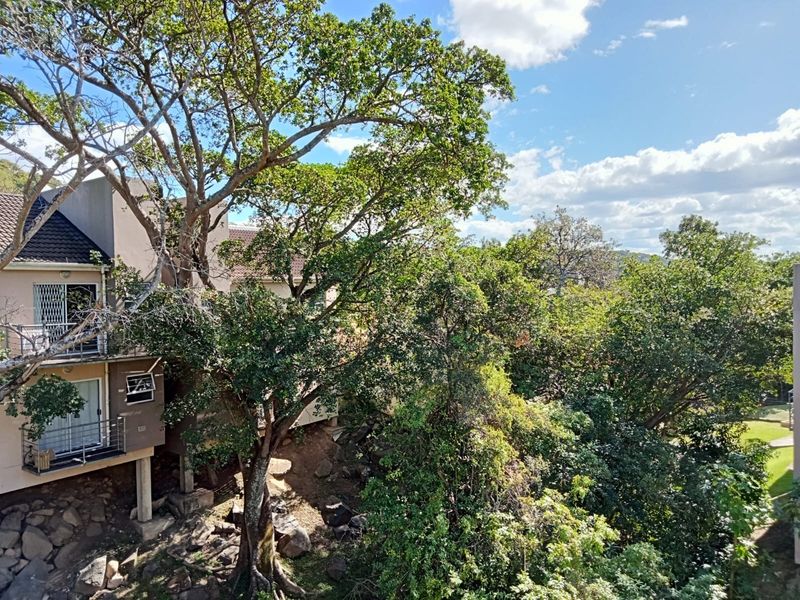 Elevated view overlooking lush mature trees and natural landscape, featuring a balcony with security gate and sliding door access.