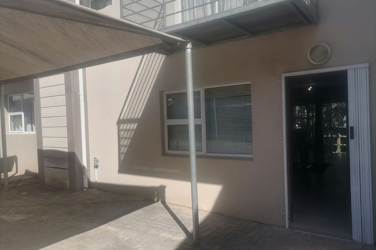 Rear exterior view of the apartment featuring a paved patio area, shade sail, and access to the interior via a sliding door.