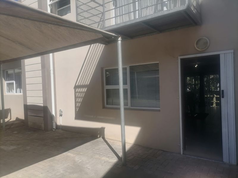 Rear exterior view of the apartment featuring a paved patio area, shade sail, and access to the interior via a sliding door.