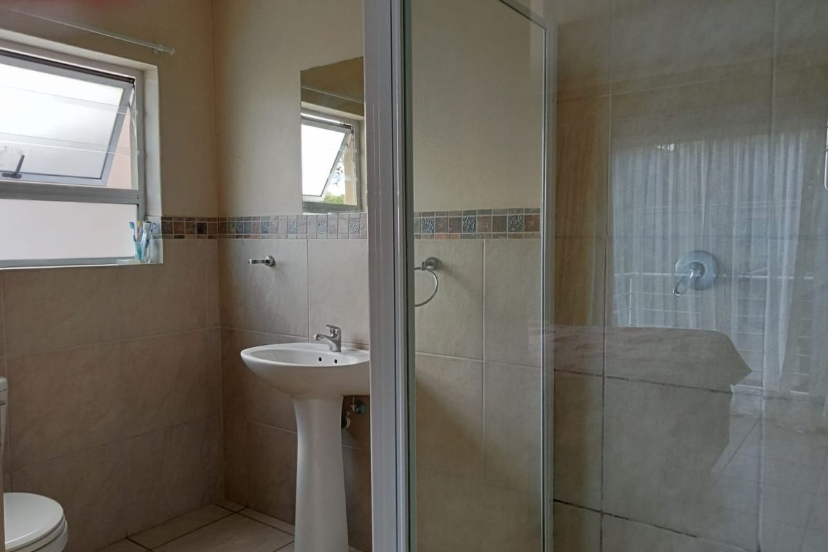 A functional bathroom featuring a pedestal basin, tiled walls, and a glass-enclosed shower unit.