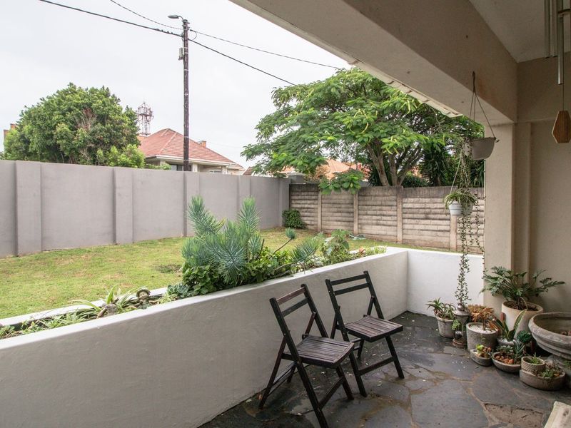 A covered patio area featuring stone flooring and a built-in planter box, overlooking a private rear garden enclosed by concrete boundary walls.