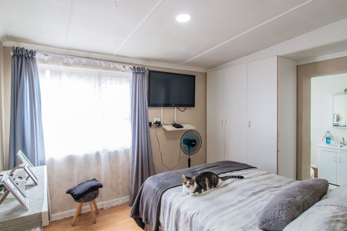 A functional bedroom featuring built-in cupboards, laminate flooring, and direct access to an en-suite bathroom with a vanity.