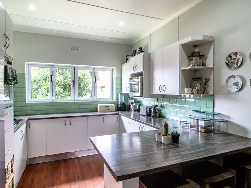 A functional kitchen featuring white cabinetry, dark laminate countertops, a light green subway tile backsplash, and built-in appliances with wood-look flooring.