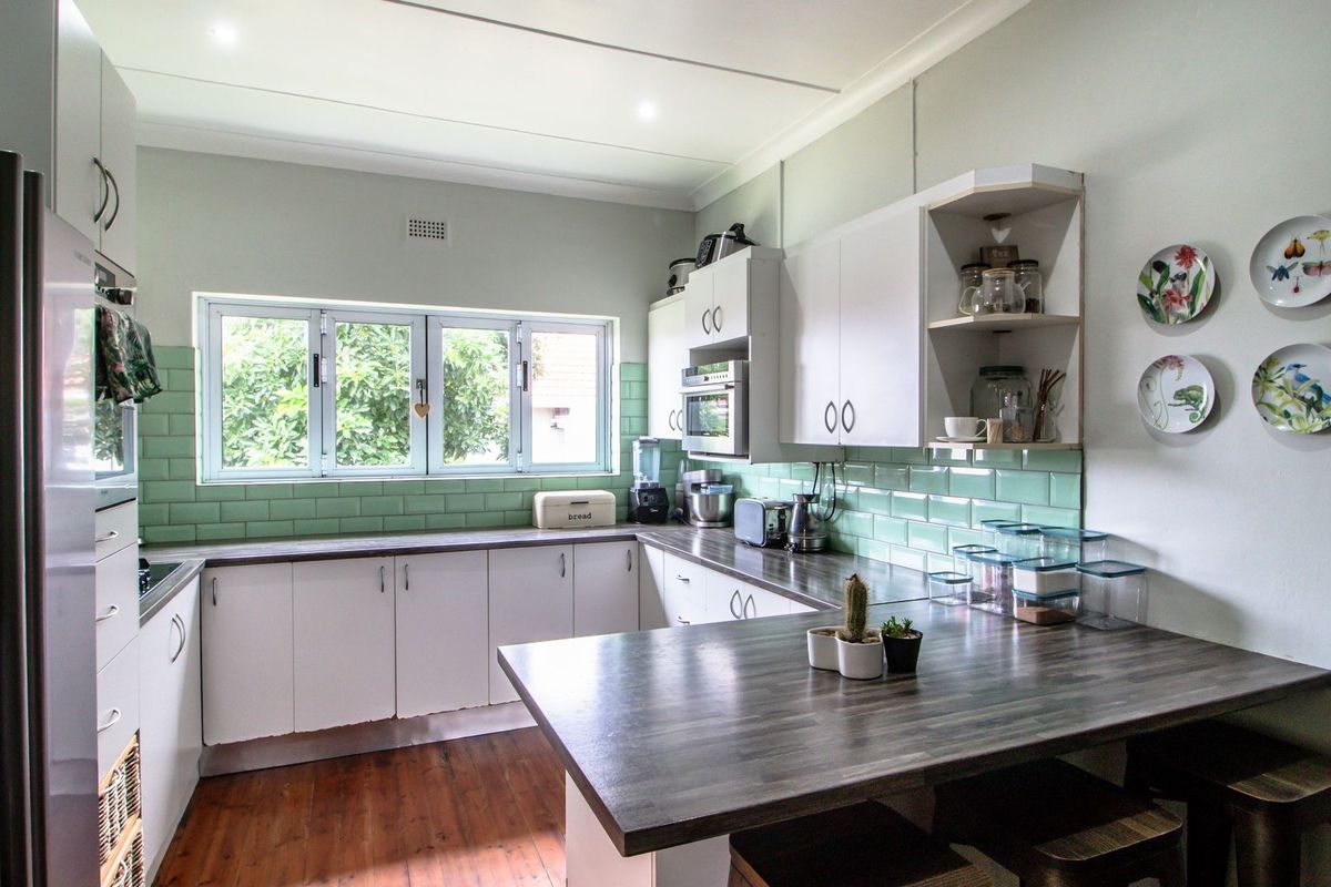 A functional kitchen featuring white cabinetry, dark laminate countertops, a light green subway tile backsplash, and built-in appliances with wood-look flooring.