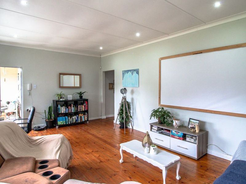 A spacious living room featuring polished hardwood flooring, recessed ceiling lighting, and a wall-mounted projection screen, creating a comfortable and functional entertainment space.
