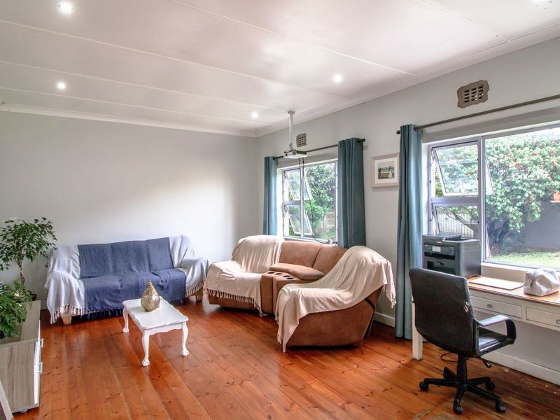 A spacious living room featuring polished timber flooring, recessed downlighting, and large aluminium windows providing natural light and garden views.
