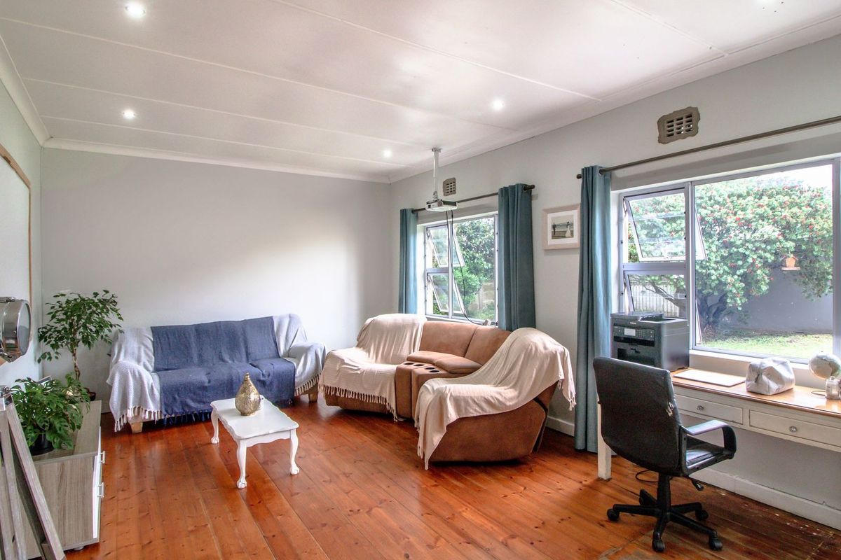 A spacious living room featuring polished timber flooring, recessed downlighting, and large aluminium windows providing natural light and garden views.
