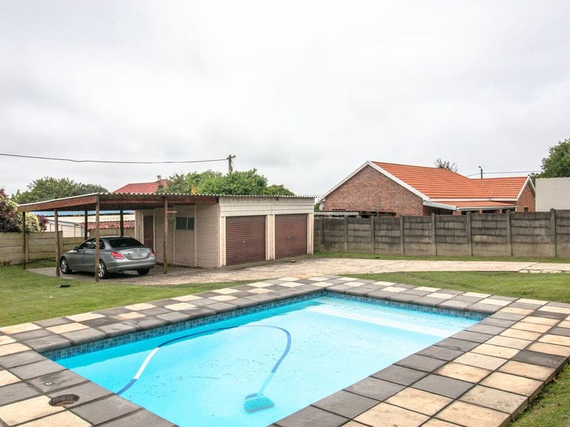 Outdoor area featuring a swimming pool with tiled surround, a double garage, and a carport set within a fenced backyard.