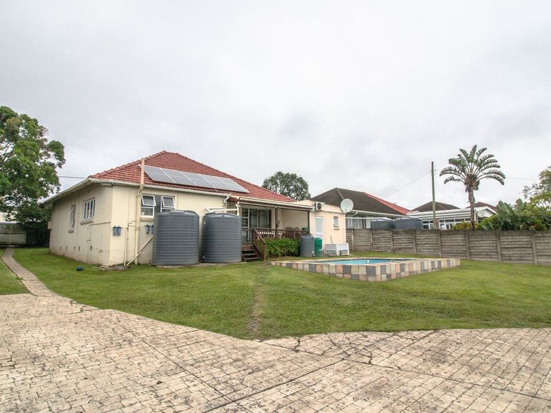Rear view of the property featuring a swimming pool, paved driveway, water storage tanks, and solar panels installed on the tiled roof.