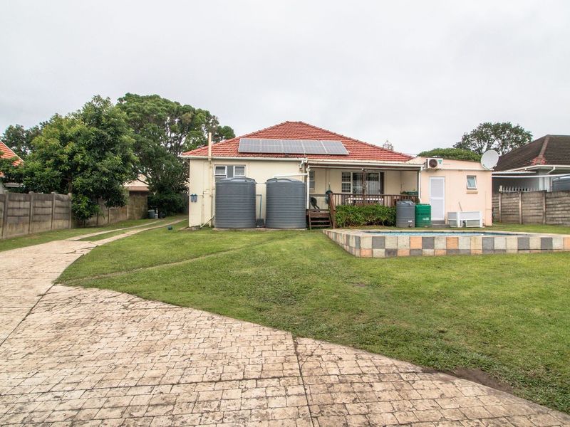 Rear view of the property featuring a swimming pool, timber deck, solar panels, and large water storage tanks set within a spacious garden.