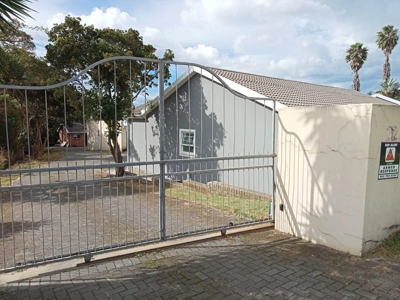 Front view of the townhouse property featuring a metal sliding gate, paved driveway, and perimeter wall with security signage.