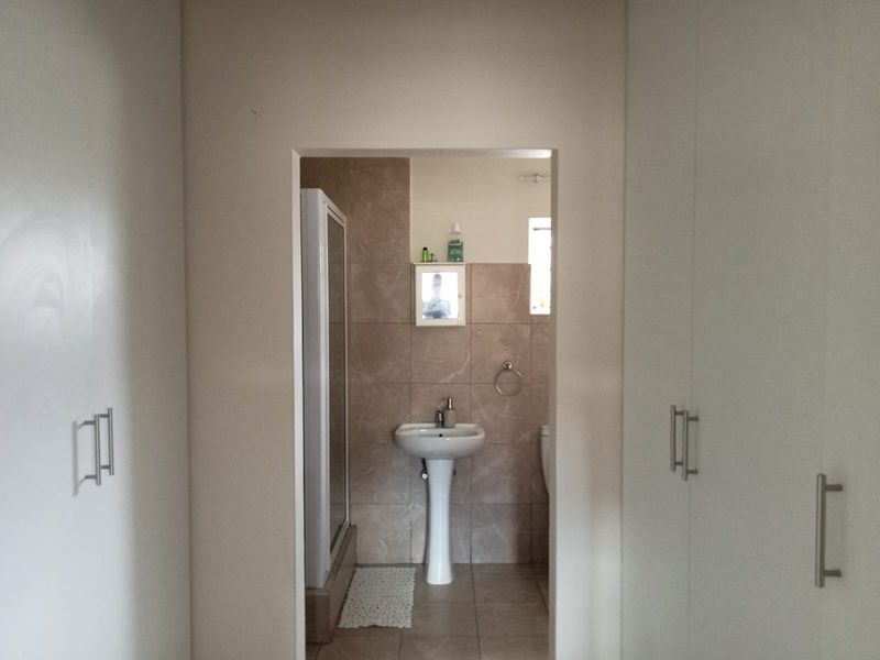 A functional bathroom featuring a pedestal basin, shower enclosure, and tiled finishes, accessed through a hallway with built-in storage cupboards.